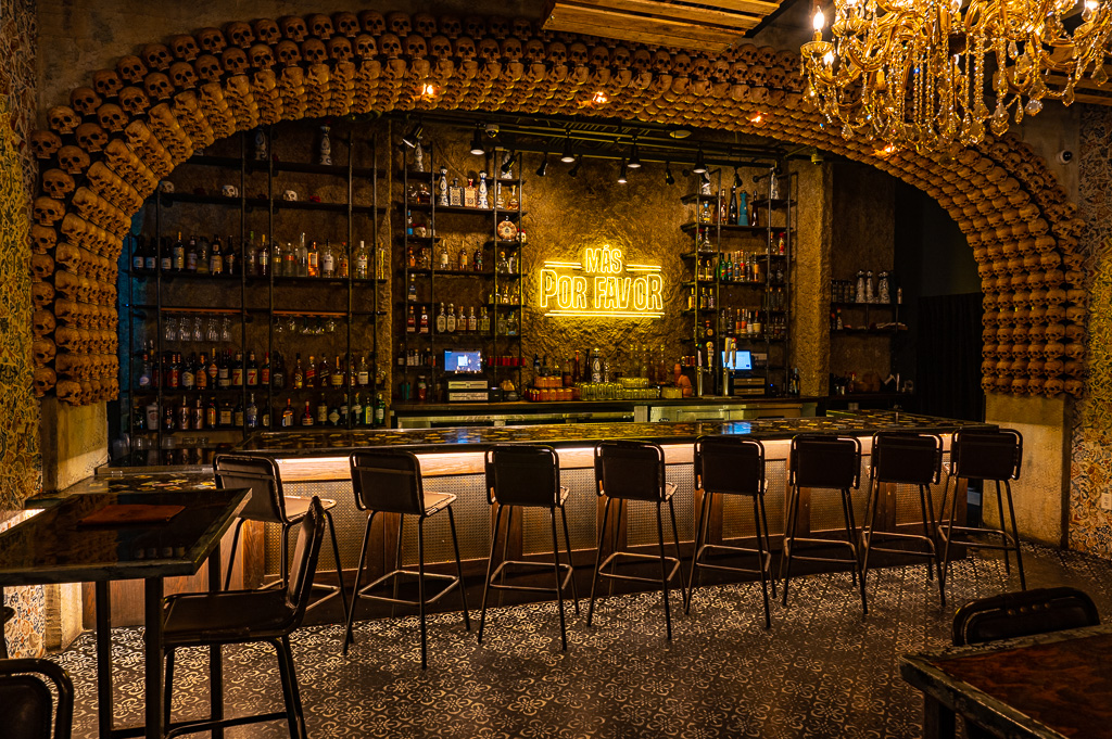 Interior of Mas Por Favor restaurant in Las Vegas featuring a stylish bar with neon sign and skull décor.